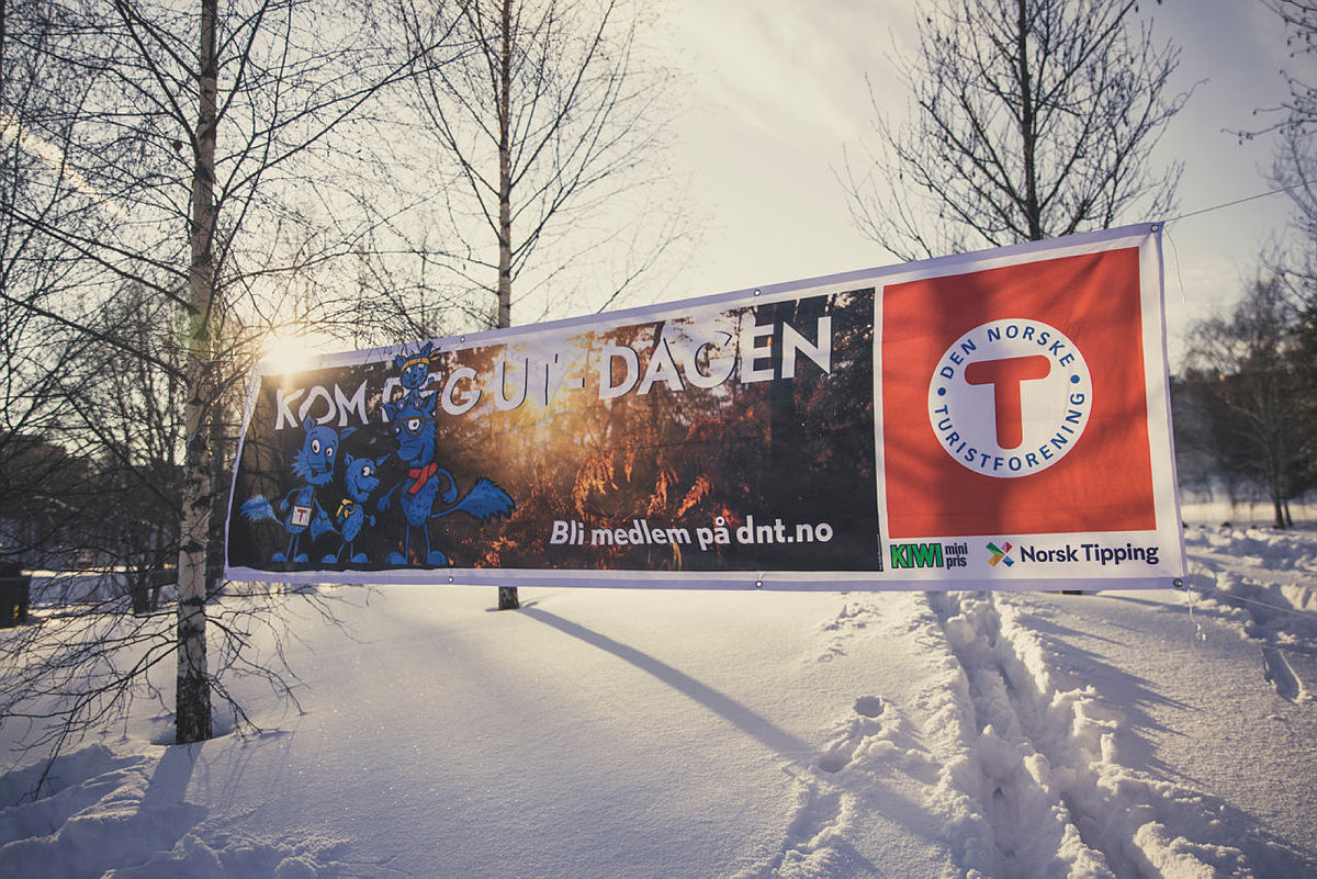 Synstolking: Bildet viser et banner der det står Kom deg ut-dagen, snø og trær.