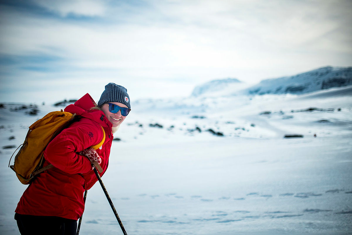 Person lener seg mot skistavene med snødekt landskap i bakgrunnen